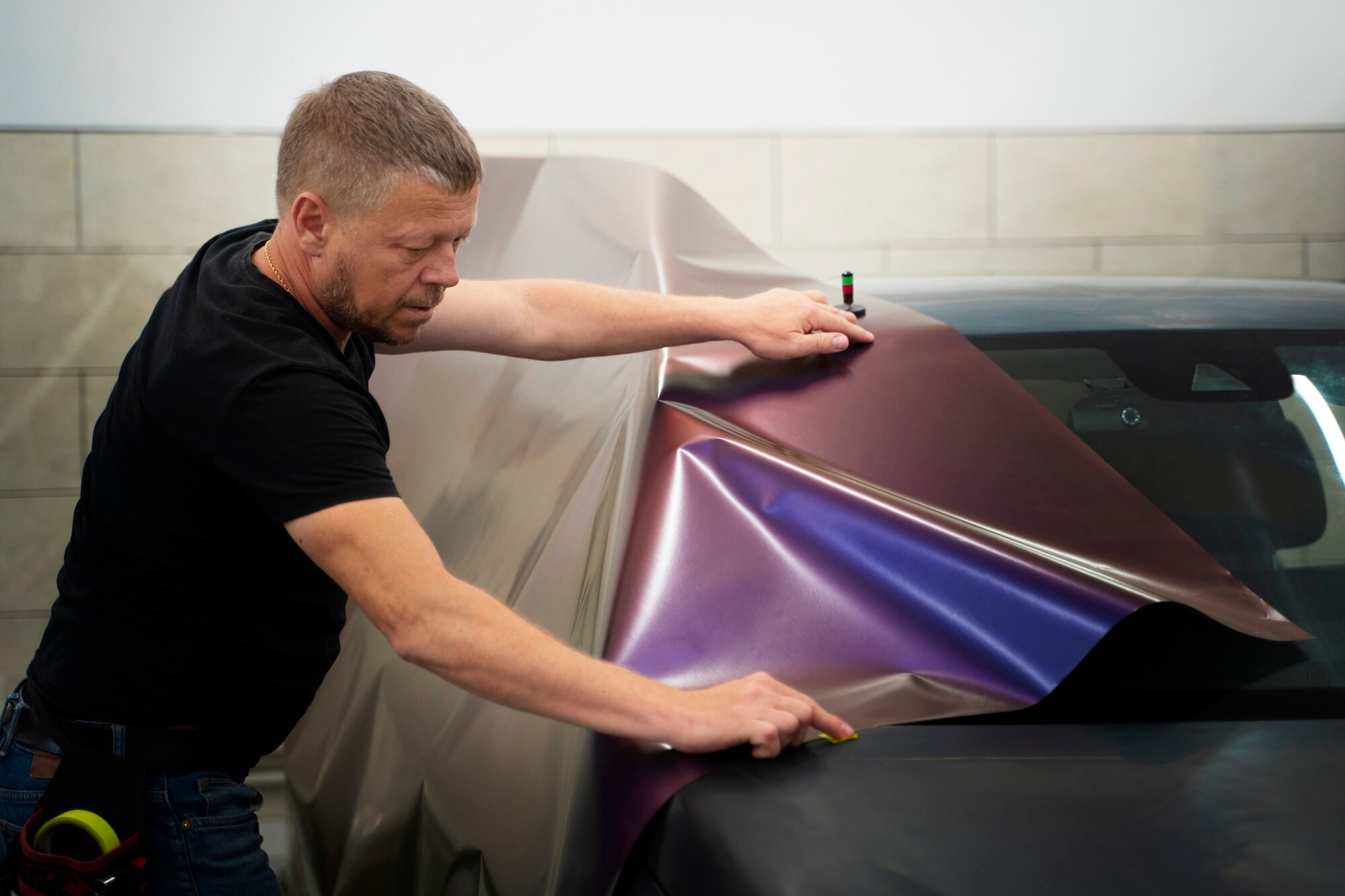 professional-male-installs-multi-colored-protective-hydrophobic-vinyl-film-on-black-car-vinyl-color-change-iPAC-Auto-Spa-Ontario-CA