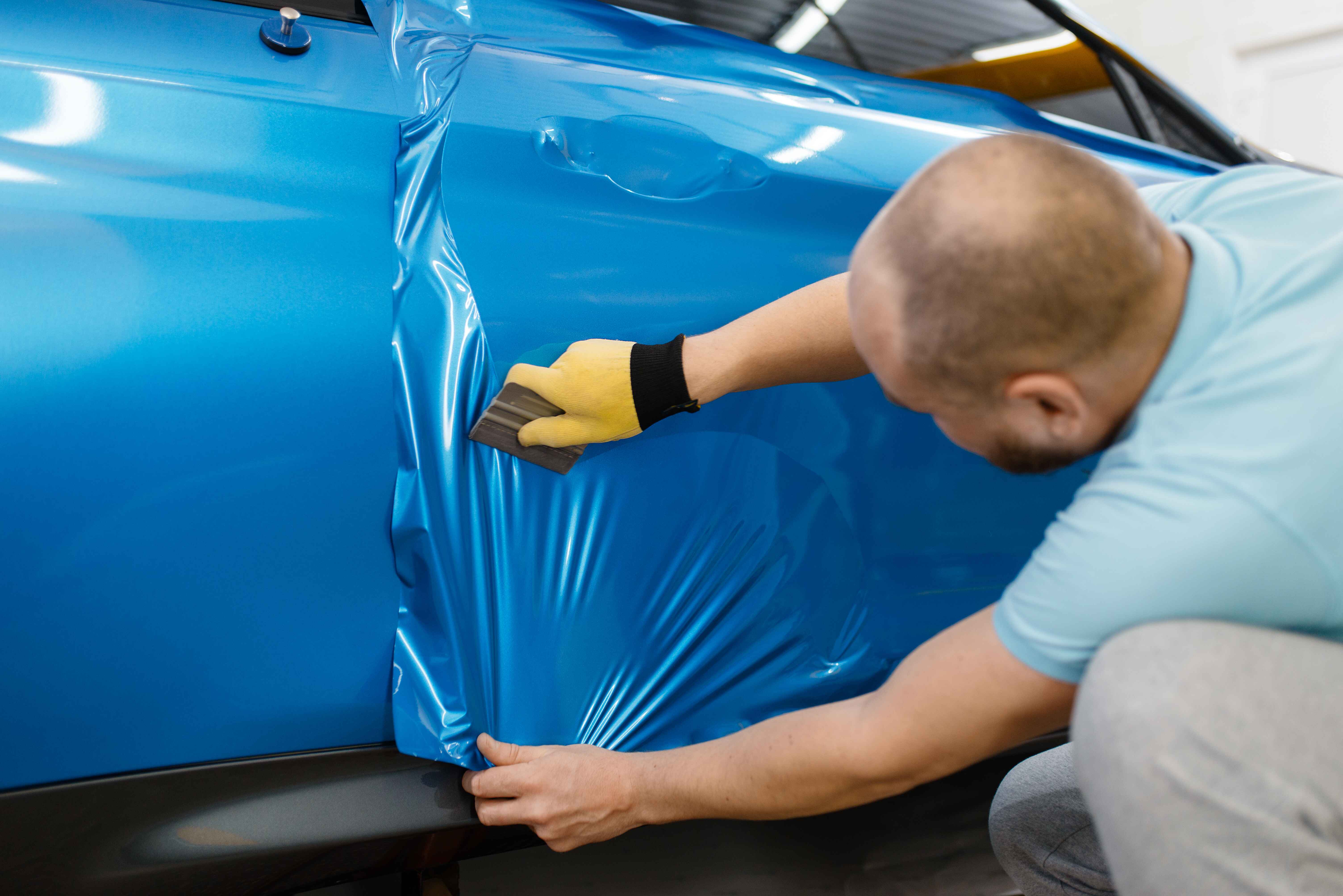 professional-male-wearing-gloves-installs-blue-protective-hydrophobic-vinyl-film-on-black-car-vinyl-color-change-iPAC-Auto-Spa-Ontario-CA